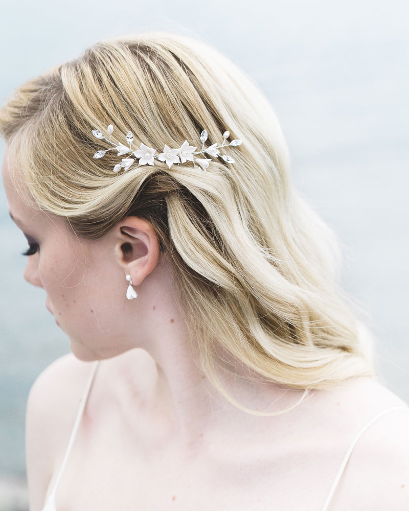 Close-up of model with blonde hair and soft waves wearing a bridal hair comb with crystals, flowers, and pearls. Pinned on the side, above the ear.