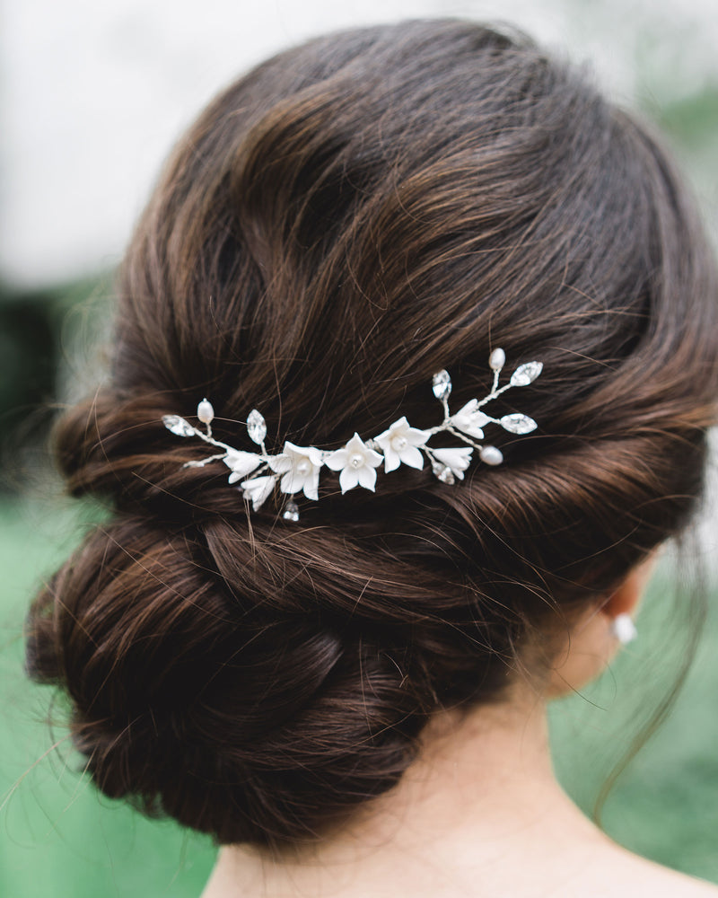 Close-up of model with dark hair and low updo wearing a bridal hair comb with crystals, flowers, and pearls