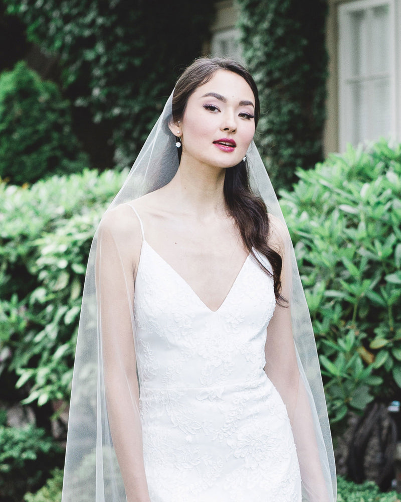 Model with dark hair and pinned back hair wearing delicate statement earrings with a long simple veil.