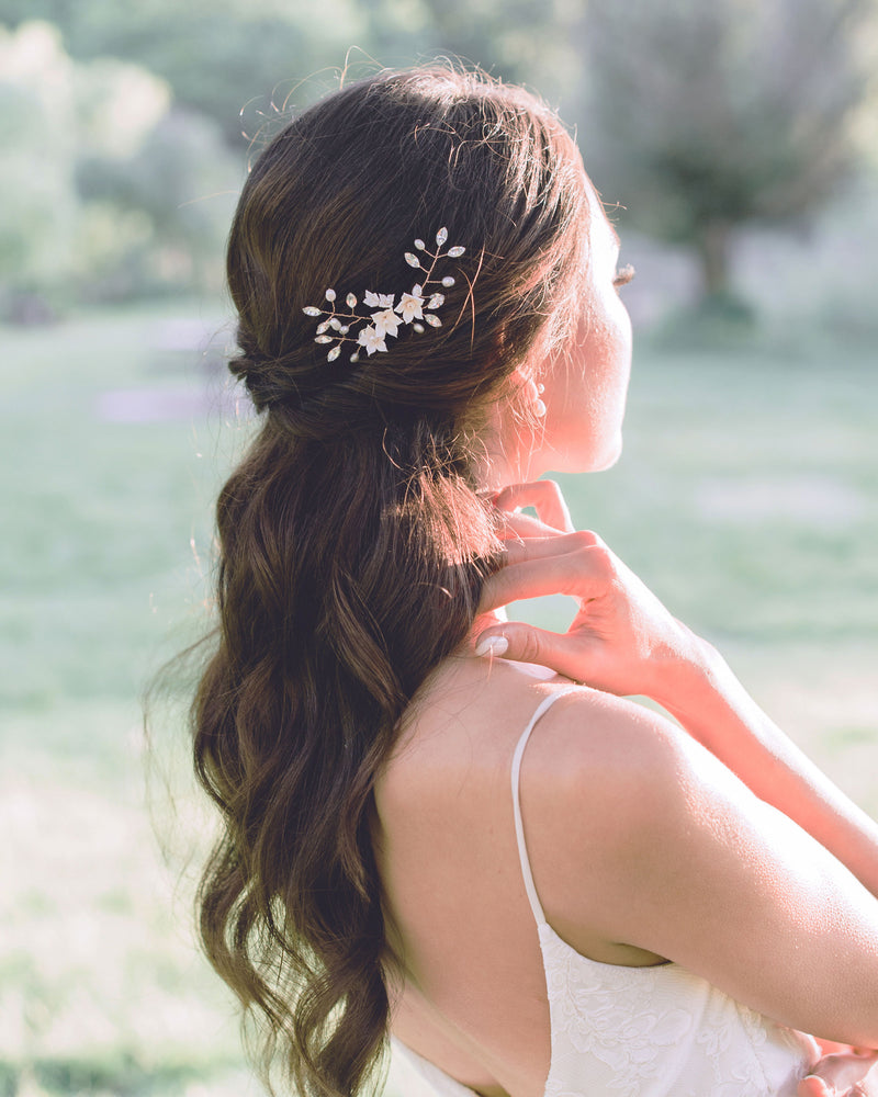 A model with long dark hair and half up hairstlye poses with her face to the setting sun. She is wearing the set of three Belle Fleur Hair Pins clustered together in her hair. The hair pins are rose gold, with blush flowers, pearls, and crystals.