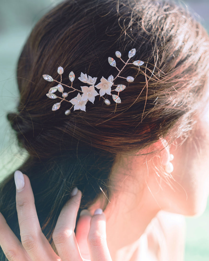 A close-up view of a model with dark hair wearing a trio of hair pins styled into her hair. The Belle Fleur Hair Pins are rose gold with blush flowers, pearls, and crystals.