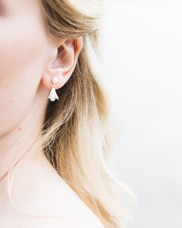 Close up on model of the Belle Fleur Petite Earrings; which feature a delicate flower hanging from a pearl stud.