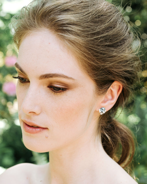 A model with a bridal updo wears silver crystal stud earrings with aquamarine crystals above a cluster of smaller crystals