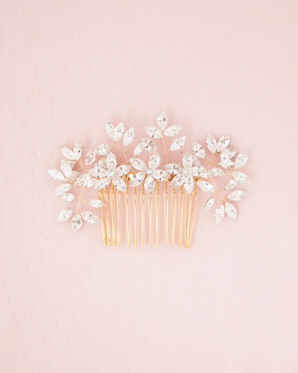 A flatlay on a pink background of the Enchanted Crystal Comb in gold.