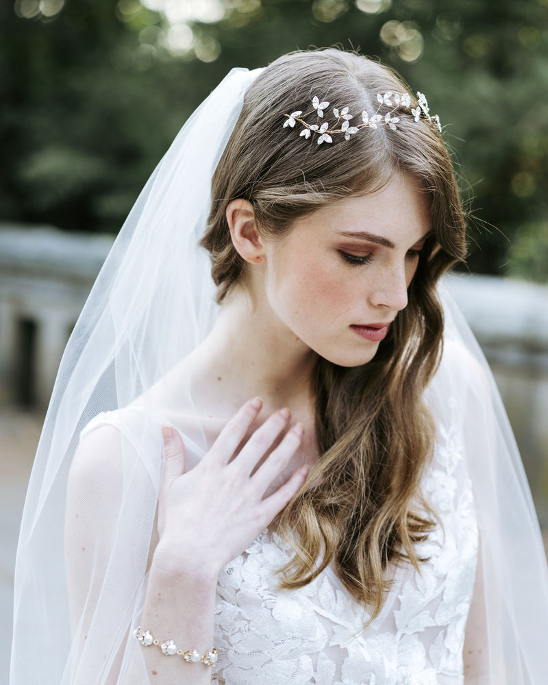 A bride wears her hair in soft waves with the Crystal Blossoms hair vine, Dainty pearl bracelet, and simple Lily Veil.