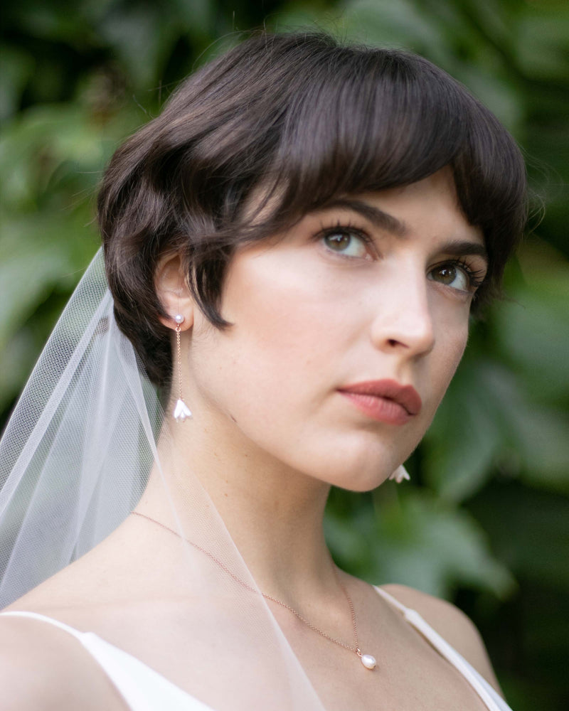 A bride with a pixie cut wears dainty flower drop earrings on a pearl stud with a matching teardrop pearl necklace..