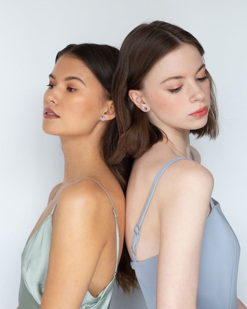 Two models wear bridesmaid jewelry. On left, she wears the Celestial Crystal Stud Earring in rose gold/tanzanite. On the right, she wears the Starry Eyed Stud Earrings in tanzanite.