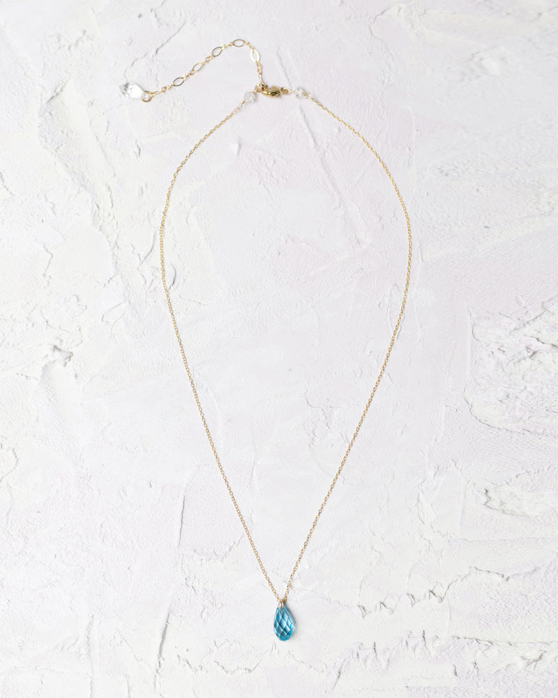 Flatlay of the Dewdrop Necklace with aquamarine crystal drop in gold.