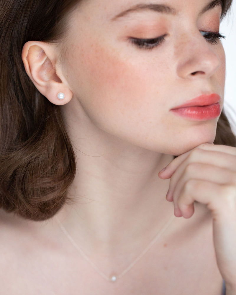 A model wears a bridal jewelry set with pearl stud earrings and a matching pearl drop necklace.