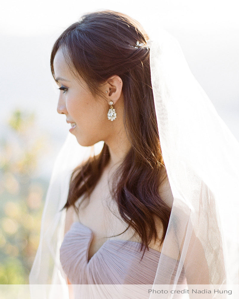 A bride wears the Petite Crystal Drop Earrings in gold, paired with a classic tulle veil.
