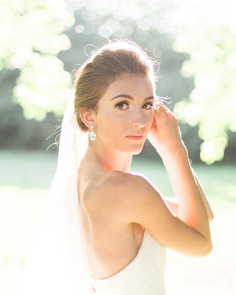 A bride wears the Petite Crystal Drop Earrings in silver, paired with a classic tulle veil.