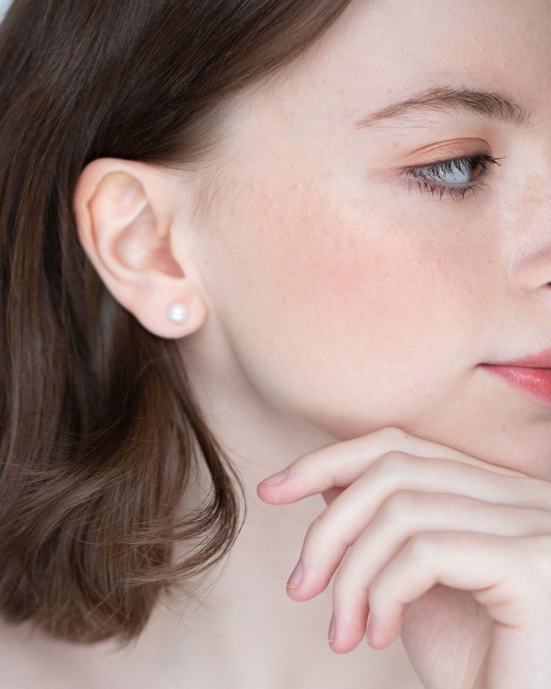 A bridesmaid wears classic pearl stud earrings in petite 6mm size.