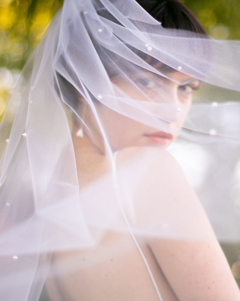 A bride gazes into the camera through a gauzy tulle veil with scattered pearls.