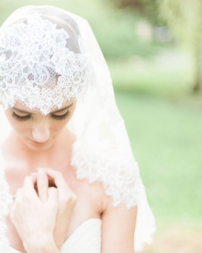 A close view of a model wearing the Analina Mantilla Fingertip Veil, which has a wide Chantilly lace detail all around.