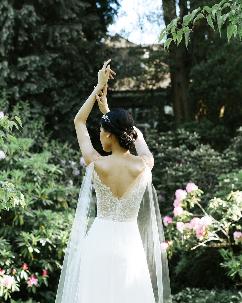 A closer back view of a bride wearing the Aster Cape Veil, which attaches to the spaghetti straps of her lace bodice.