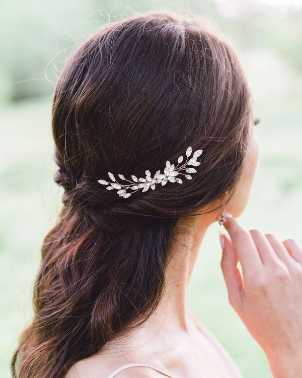 A dark-haired model with a half-up bridal hairstyle wears the Aster Comb in rose gold and crystal.