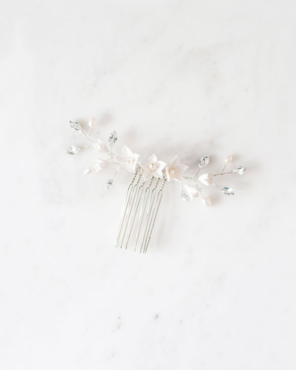 Flatlay photo of silver bridal hair comb with crystals, white flowers, and pearls