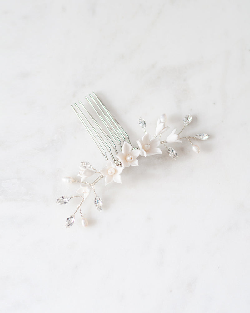 Flatlay photo of silver bridal hair comb with crystals, white flowers, and pearls