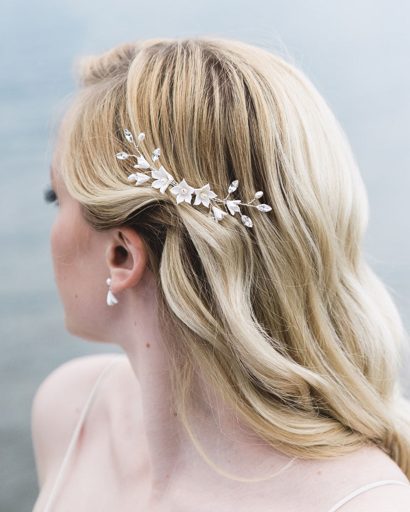 Close-up of model with blonde hair and soft waves wearing a bridal hair comb with crystals, flowers, and pearls. Pinned on the side, above the ear.