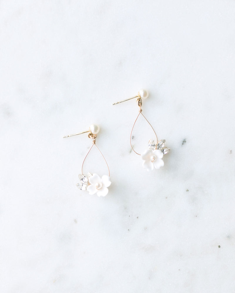 Flat lay of hand-crafted statement earrings with delicate wire teardrop, small white flower and crystals hanging from a pearl stud.