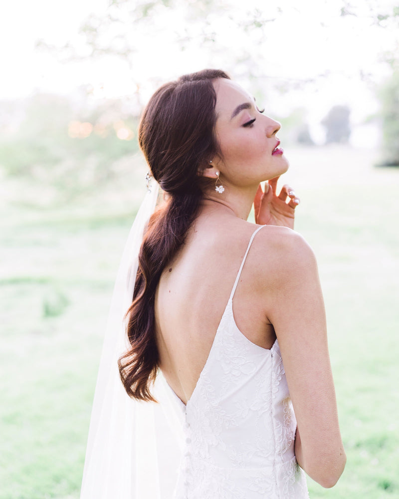 Model posing during golden hour. She has dark hair and a dark red lip and is wearing the Belle Fleur Earrings with rose gold wire, blush flowers, and crystal accents.