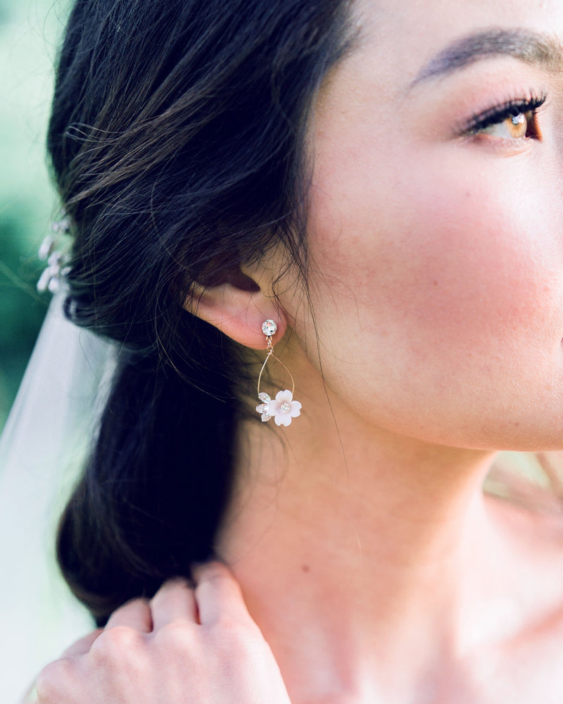 A close-up of a model with dark hair wearing the Belle Fleur delicate statement earrings in rose gold, with blush flowers and all crystal.