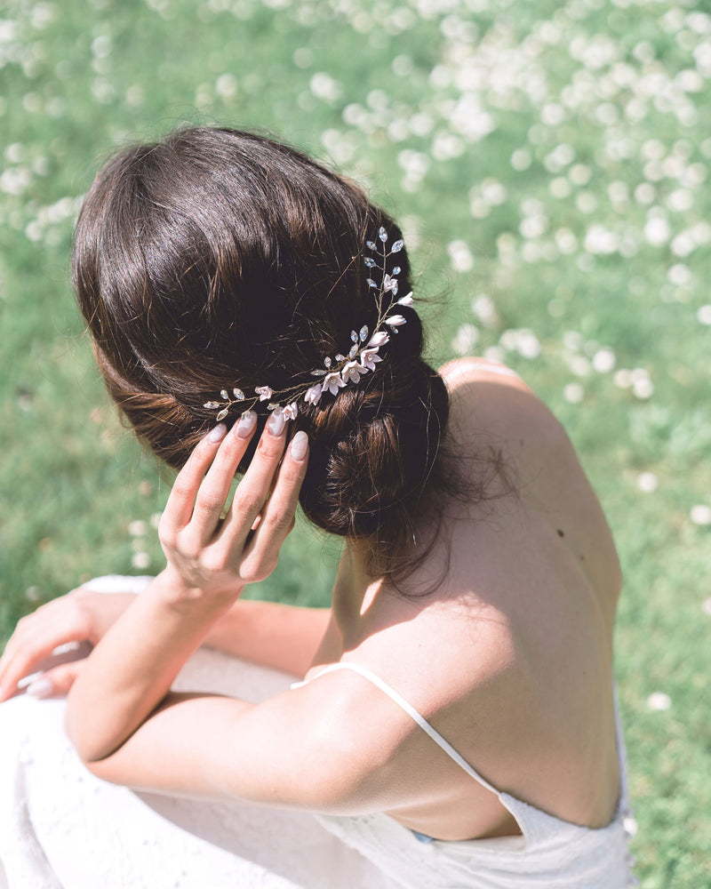 A back view of a model with dark hair wearing the Belle Fleur grand Comb above a low updo. The comb is gold with blush flowers and lots of crystals.