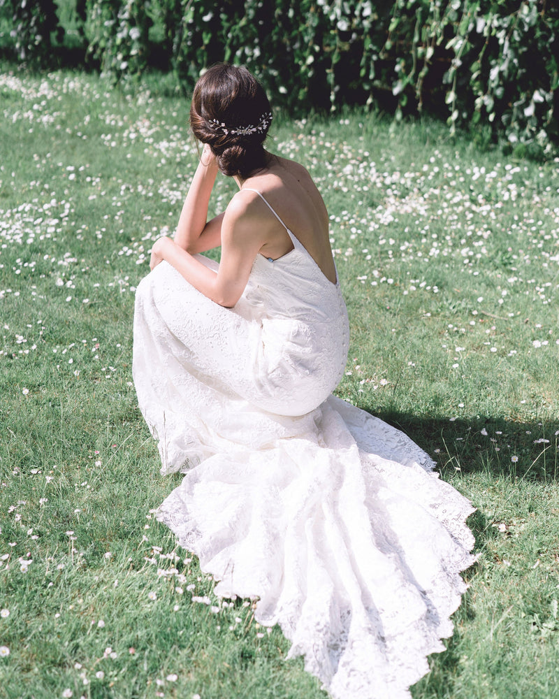 A model poses  in a grassy field. She is wearing a low bridal updo with a dramatic comb in the back.