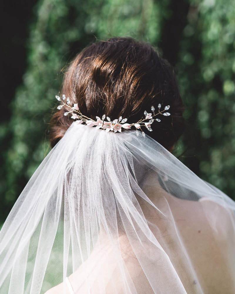 A back view of a model with dark hair wearing the Belle Fleur grand Comb above a bridal veil. The comb is gold with blush flowers and lots of crystals.