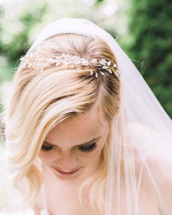 A model with blonde hair and loose waves looks down to show the Belle Fleur Grand Comb styled as a crown on the top of her head. It is style alongside a simple veil.