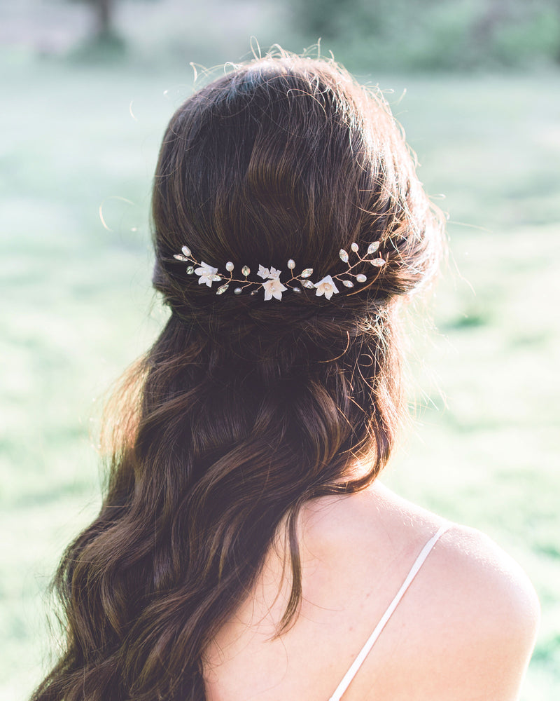 A back view of a model with long dark hair wearing a trio of hair pins in her half up hair. The hair pins have been placed along the back of her updo, so that it styles across the back of her hair. The hair pins are rose gold, with blush flowers, pearls, and crystals.