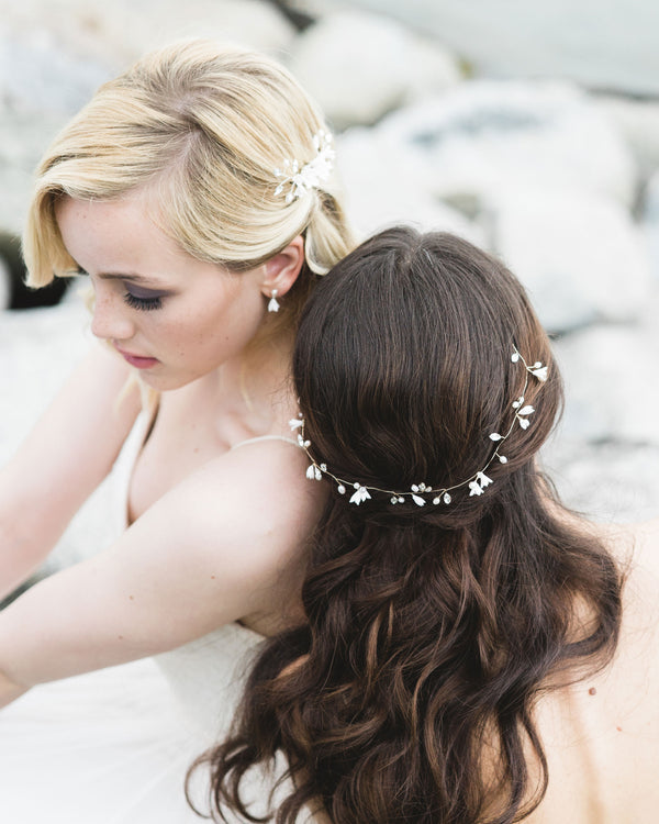 Two models pose on the rocky shore. They are wearing bridal accesories; the blonde model on the left wears small flower drop earrings and the dark-haired model on the right wears the Belle Fleur Hair Vine styled across the back of her half-up hairdo.