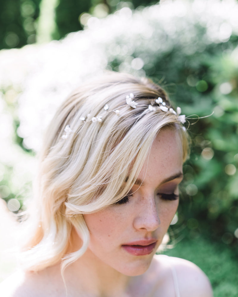 A slight top view of a model wearing the Belle Fleur Hair Vine. She is gazing downwards and hints of dainty pearls, flowers, and crystals can be seen.