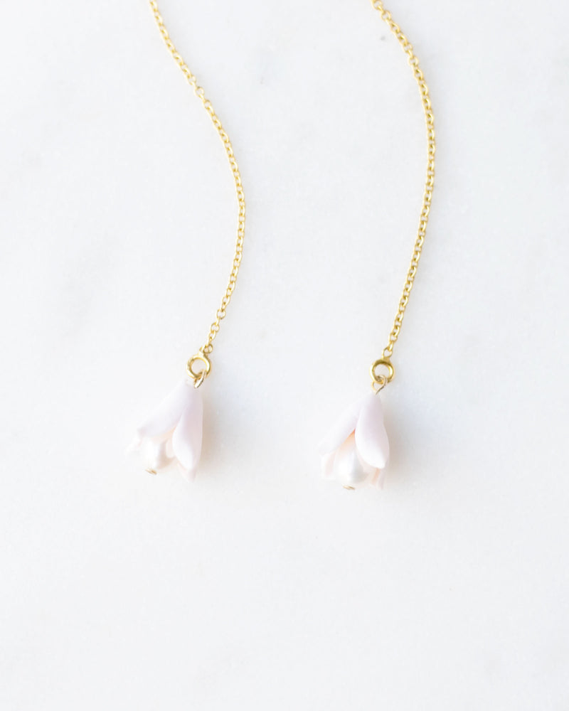 Close-up flatlay of delicate gold ear threader bridal earrings with tiny blush polymer clay flower drops.