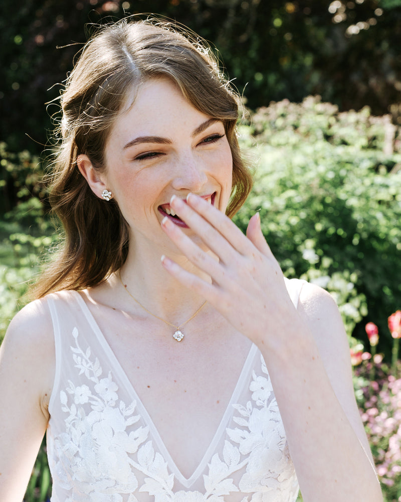 A model with auburn hair is wearing a bridal jewelry set; she wears the Celestial Crystal Drop Necklace in gold and the matching crystal stud bridal earrings.