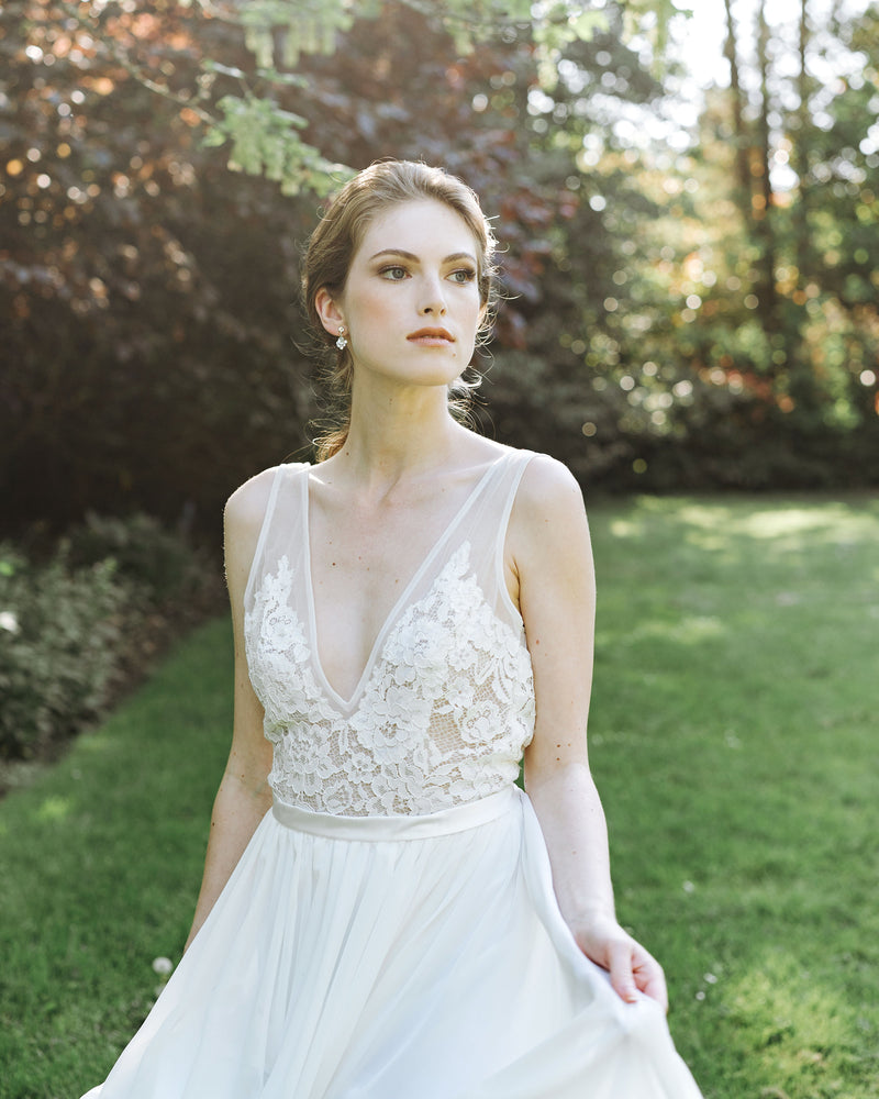 A model in a wedding dress stands in a field at Aberthau Manor; she is wearing the Celestial Crystal Drop Earrings in silver.
