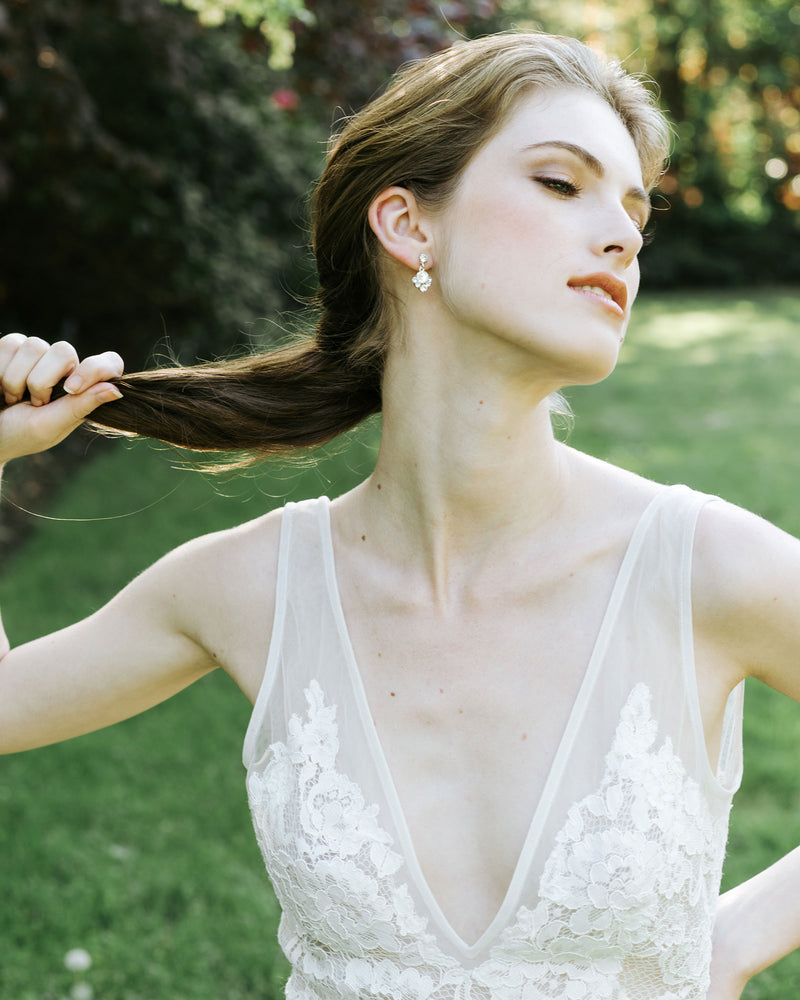 A model with a low pony poses in a wedding dress. She is wearing the Celestial Crystal Drop Earrings in silver, all crystal.