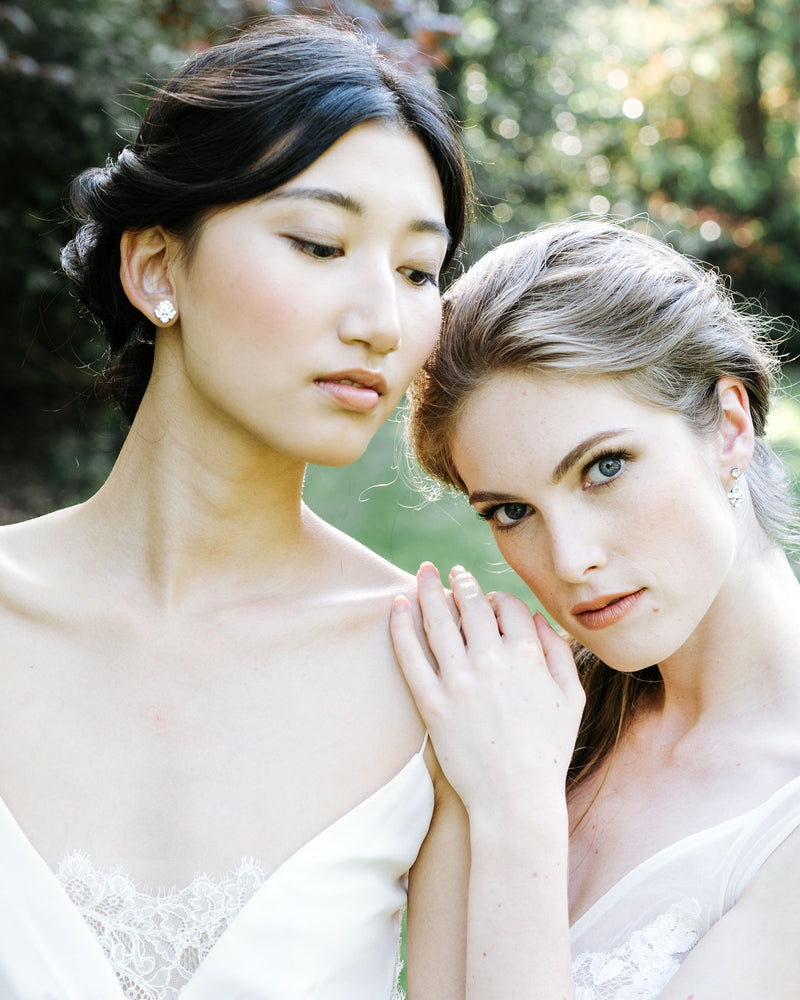 Two models pose with bridal updos. The model on left wears the Celestial Crystal Cluster Stud Earrings and the model on right wears the drop version.