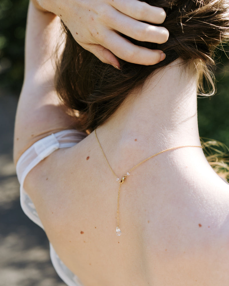 A back view of a model wearing our Celestial Crystal Drop Necklace, showing the dainty crystal drop at the back.