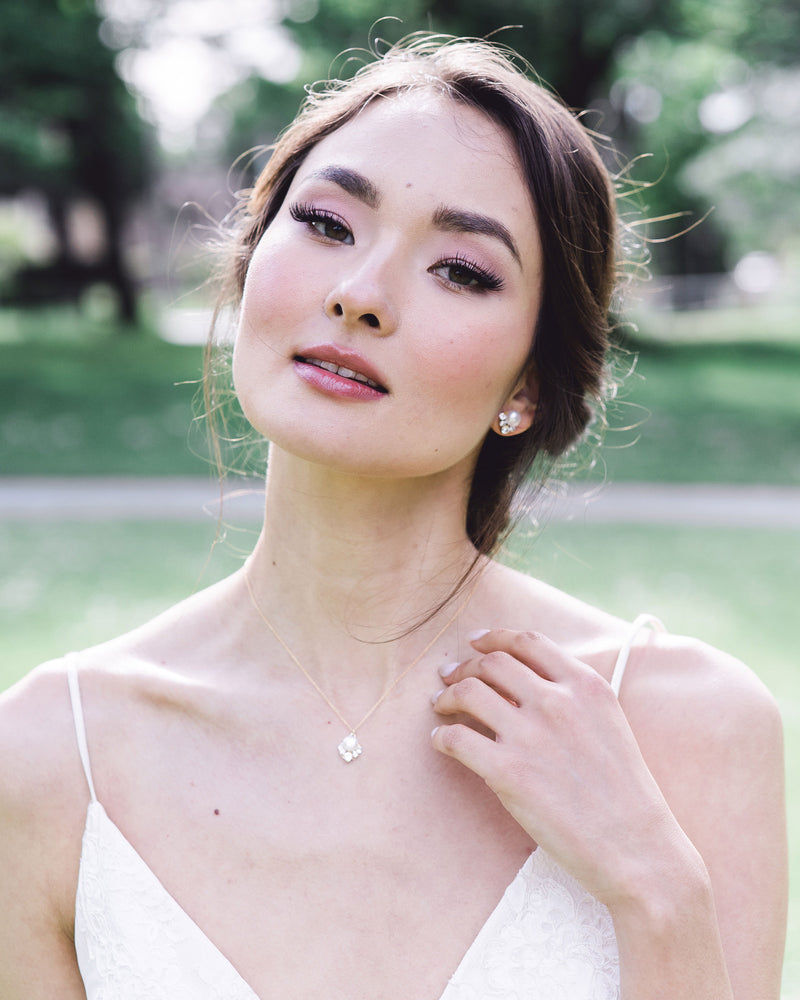 A model with dark hair and bridal makeup wears the Celestial Pearl Jewelry Set with a drop pearl necklace and matching pearl stud earrings in gold with freshwater pearls.