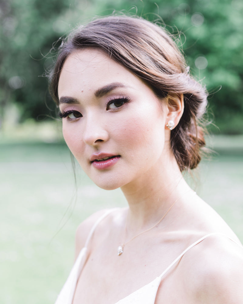 A model with dark hair and bridal makeup wears the Celestial Pearl Jewelry Set with a drop pearl necklace and matching pearl stud earrings in gold with freshwater pearls.