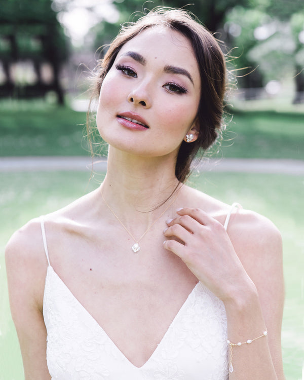 A model in a wedding dress is wearing the Celestial Pearl Jewelry Set with a dainty pearl bracelet. The necklace has a pearl drop pendant and she wears matching stud earrings in gold with freshwater pearl.