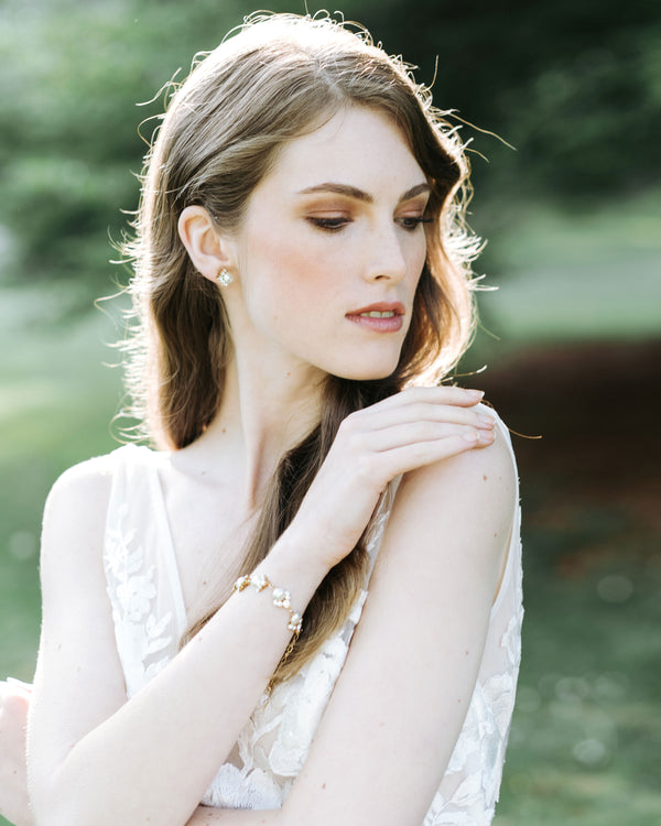 A model poses in a wedding dress, wearing the Celestial Pearl Cluster Bracelet in gold and matching pearl stud earrings.
