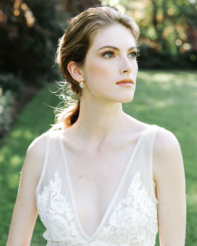 A model stands in a sun-filled field in a wedding dress. She is wearing the Celestial Pearl Drop Earrings in silver with white pearls.