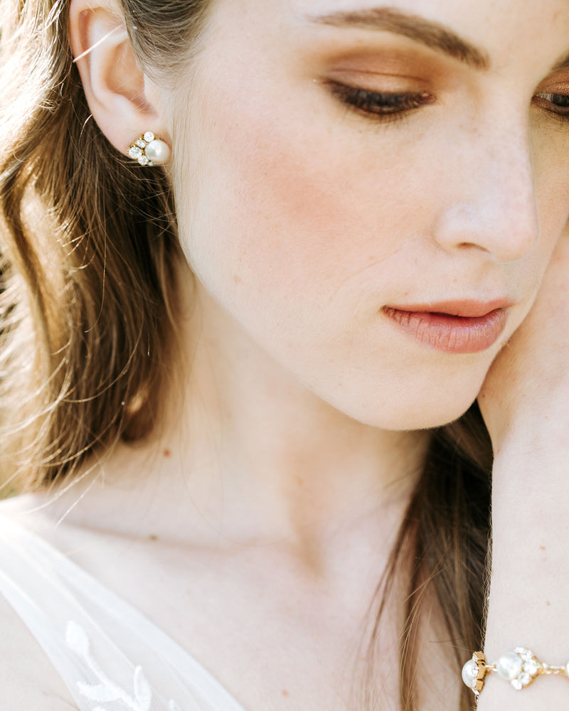 A close view of an auburn haired model wearing the Celestial Pearl Cluster Earrings in gold with cream pearls. The crystal clusters are styled to the side, instead of beneath the pearl.