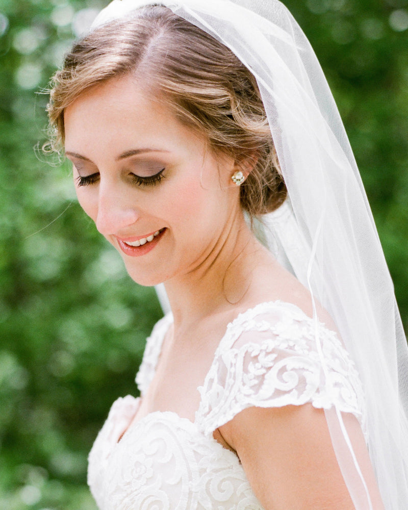 A bride is wearing the Celestial Pearl Cluster Earrings in silver cream and the Leila Ribbon Veil.