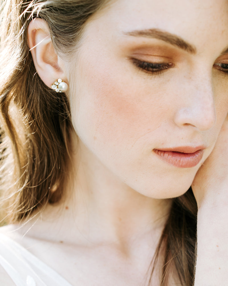 A close up on a model wearing the Celestial Pearl Cluster Earrings in gold with cream faux pearls. She is wearing them with the crystals to the side, instead of to the bottom..
