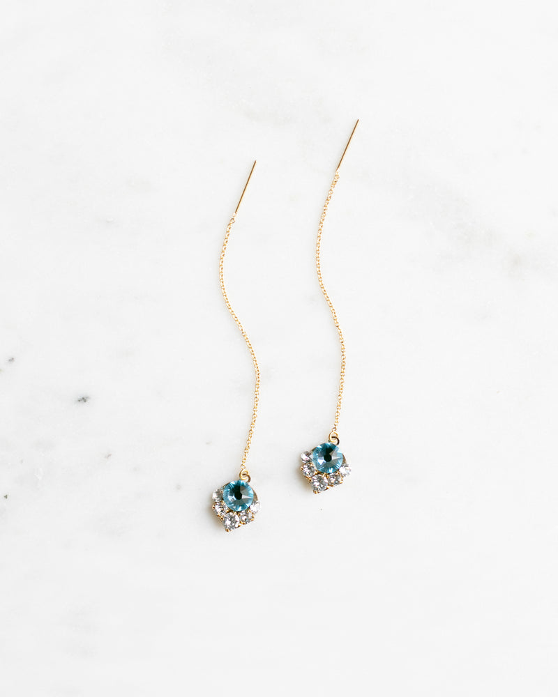 A flatlay view of the Celestial Crystal Threader Earrings in gold with aquamarine crystals.