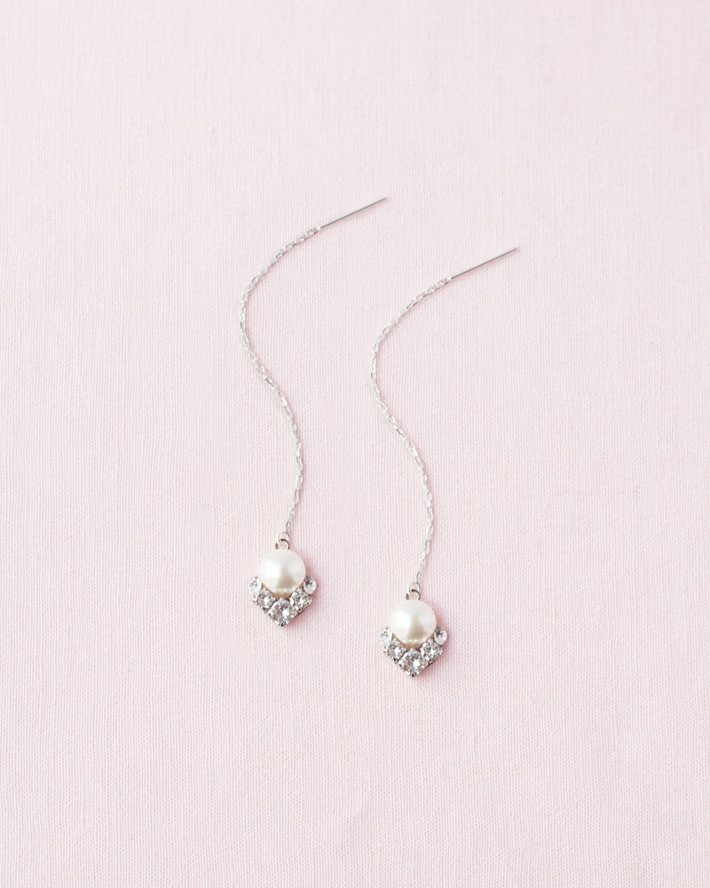 A flatlay view of the Celestial Pearl Threader Earrings in silver with cream pearls.