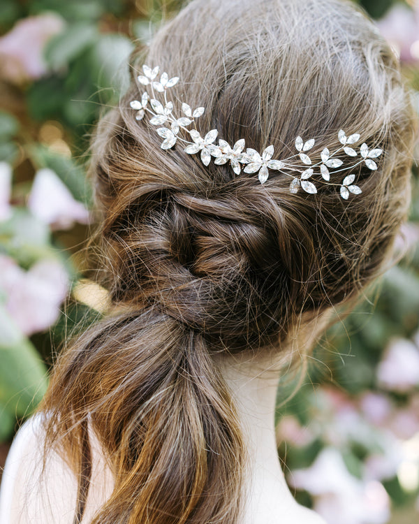 A model with a braided bridal hairstyle wears a dramatic crystal comb with crystal leaf details at the back.